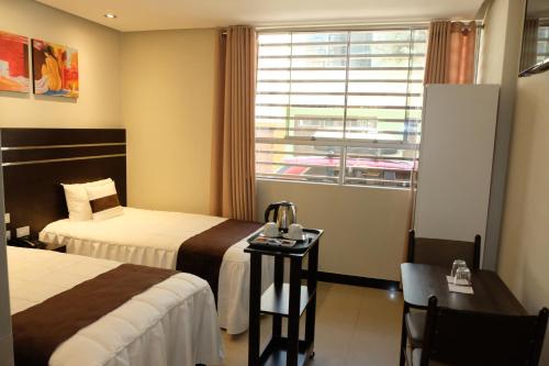 Habitación de hotel con 2 camas, mesa y ventana en Hotel Puma'r Tacna en Tacna