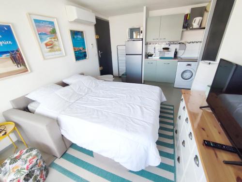a bedroom with a white bed and a kitchen at Appartement Plage des Arts in Saint-Cyprien