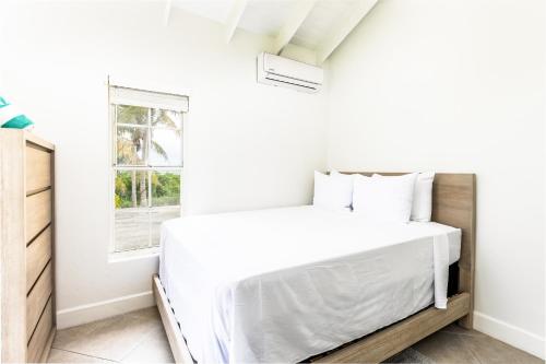 a white bedroom with a bed and a window at NEW Tropical Bottle Creek Stay Beach 5 min Drive in NCA