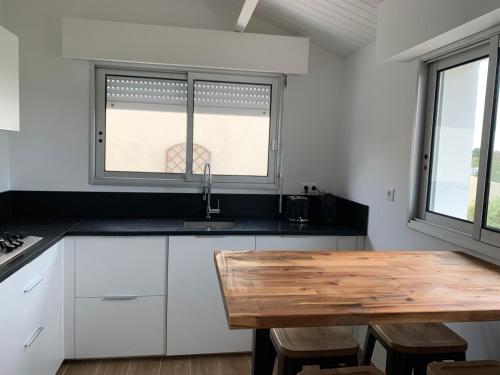 - une cuisine avec une table en bois et 2 fenêtres dans l'établissement villa plage les Sables d’Olonne, à La Chaume