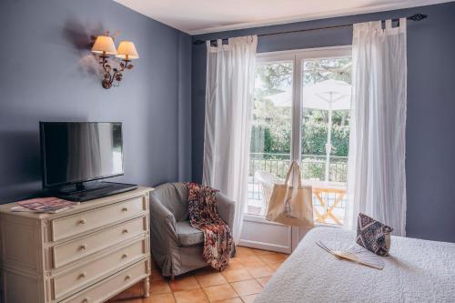 ein Schlafzimmer mit einem TV, einem Stuhl und einem Fenster in der Unterkunft La Villa d'Andrea in Ramatuelle