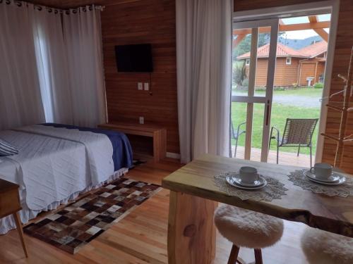 1 dormitorio con cama, mesa y ventana en Pousada Caminhos do Mel - Urubici - SC, en Urubici
