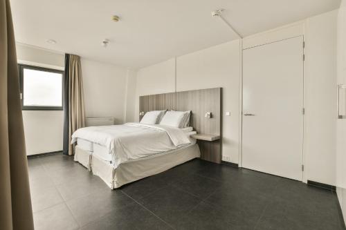 a bedroom with a large white bed and a window at Appartement met frontaal zeezicht in Bloemendaal in Bloemendaal