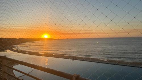 una puesta de sol sobre el océano con una valla en Departamento San alfonso del mar, en Algarrobo