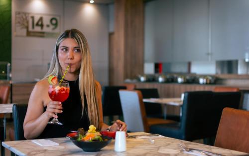 a woman sitting at a table with a drink at Hotel Mocawa Plaza Armenia in Armenia