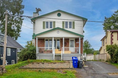 a white house with a porch and a yard at Riviera Escape on Waterfront with Hot Tub in Gatineau