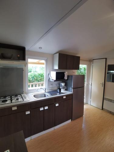 d'une cuisine avec des placards bruns, un évier et une fenêtre. dans l'établissement Mobil-home dans le calme du Domaine de Lanniron R24, à Quimper