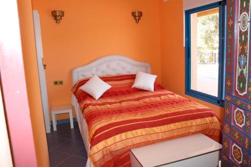 een slaapkamer met een bed met oranje muren en een raam bij Dar Nfis piscine hydro massage Privée, jet ski, Agafay in Lalla Takerkoust