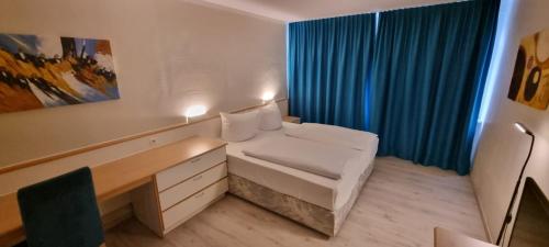 Hotel B99 في أوفنباخ: غرفة بسرير ومكتب وستارة زرقاء
