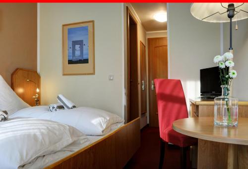 ドレスデンにあるElbterrasse Wachwitzのベッド、テーブル、赤い椅子が備わるホテルルームです。