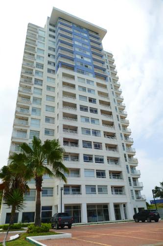 een groot wit gebouw met palmbomen ervoor bij Ecusuites playas torre pacific ll in Guayaquil