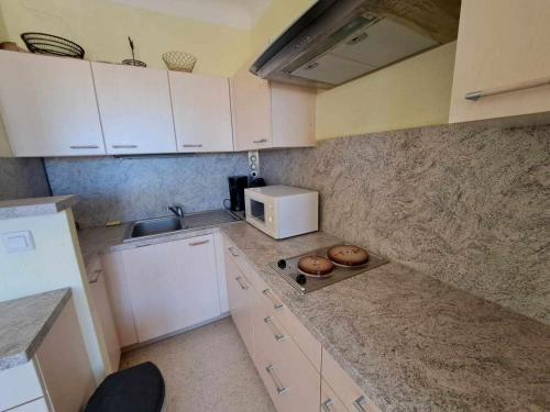 une petite cuisine avec des armoires blanches et un micro-ondes dans l'établissement Charmant T2 en RDC, 2 pas de la plage, terrasse, parking privé, tout équipé! - FR-1-326-811, à Marseillan