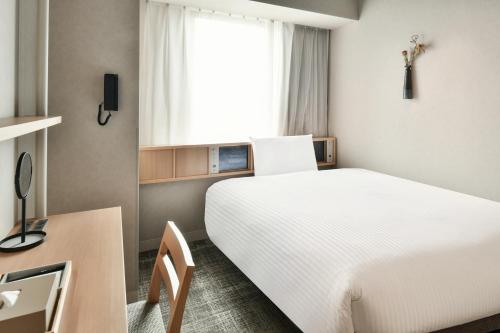 松山市にあるREF Matsuyama City Station by VESSEL HOTELSの白いベッドとデスクが備わるホテルルームです。