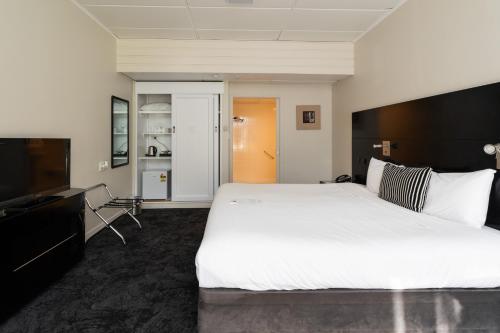 a bedroom with a large bed and a flat screen tv at Hotel Armitage and Conference Centre in Tauranga