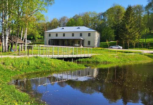 eine weiße Scheune mit einer Brücke über einen Fluss in der Unterkunft Inovatorių slėnis/ Innovators' valley in Antalieptė