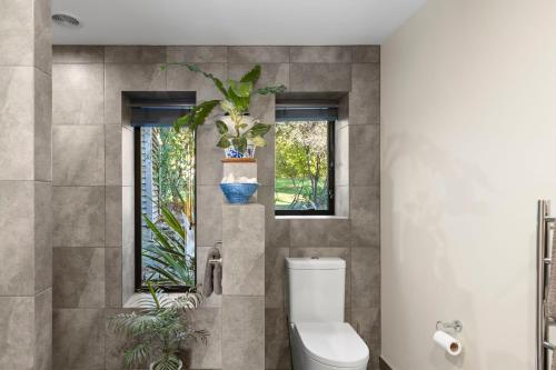a bathroom with a toilet and two windows at Supplejack Gardens in Upper Moutere