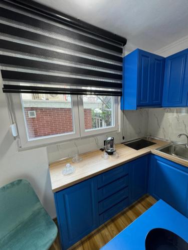 Keli’s apartment في تيرانا: مطبخ مع دواليب زرقاء ونافذة مع ستارة سوداء