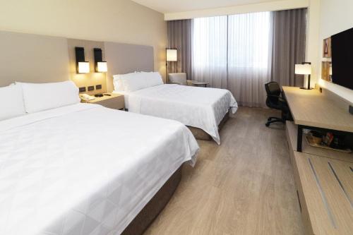 a hotel room with two beds and a desk at Holiday Inn Monterrey-Parque Fundidora by IHG in Monterrey