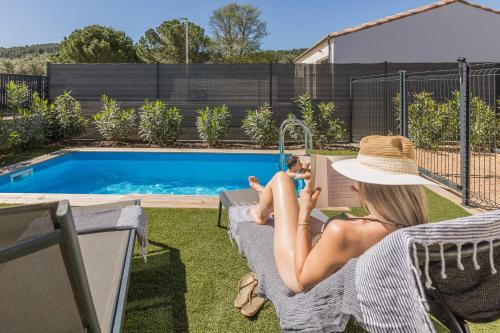 Eine Frau auf einem Stuhl neben einem Pool in der Unterkunft ღ L'Orb Enchanté - Piscine chauffée, Clim, Netflix in Cessenon