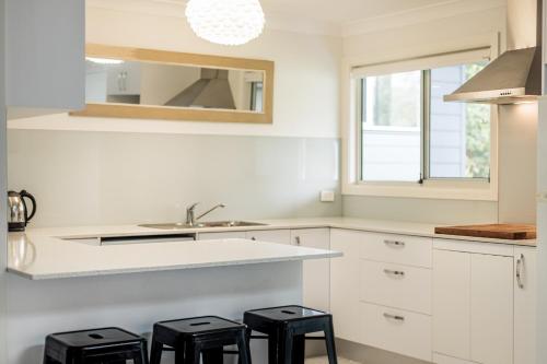 uma cozinha com armários brancos, um lavatório e bancos em Anais Hat Head em Hat Head