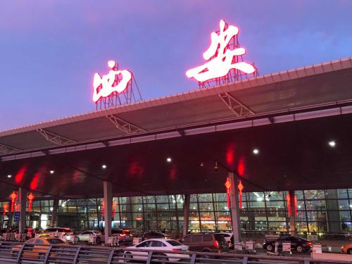 Xi'an Xianyang International Airport Space Capsule Hotel في شيان: موقف للسيارات مع لافتات نيون فوق المبنى