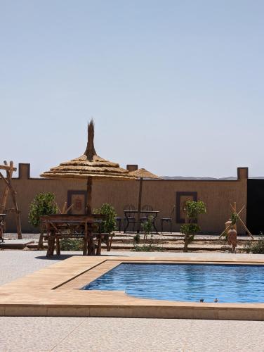 a swimming pool with a table and an umbrella at Riad Merzouga Dunes in Merzouga
