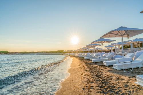 スペッキオッラにあるInfinito Resortの白いラウンジチェアとパラソル付きのビーチ