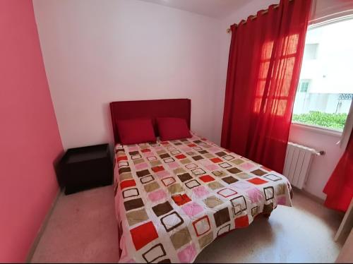 a bedroom with a bed with a red bedspread and a window at Ennasr 2 - Rez-de-Chaussée Chaleureux - Internet Fibre - Chaines International - Commerces et Services à Proximité - Service Navette in Ariana
