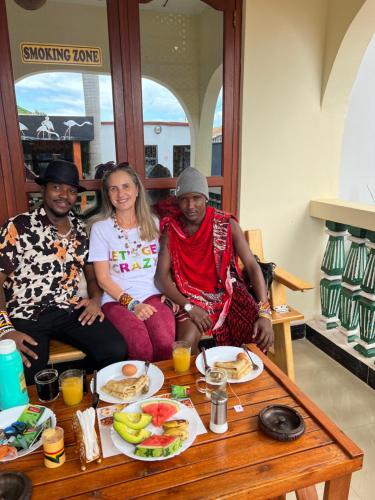 Kilimanjaro Trekcity Hostel في موشي: مجموعة من ثلاثة أشخاص يجلسون حول طاولة طعام