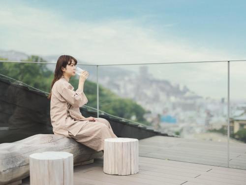 a woman sitting on a ledge drinking from a cup at SOKI ATAMI in Atami