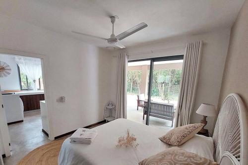 a bedroom with a white bed with a ceiling fan at AO Cottage in Petite Case Noyale