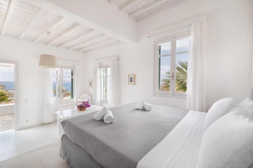 a white bedroom with a large bed with windows at Fos Apartments Mykonos in Agios Ioannis Mykonos