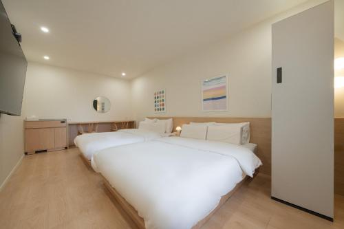 a white bedroom with two beds and a television at Aank Hotel Cheonan Station 2nd in Cheonan