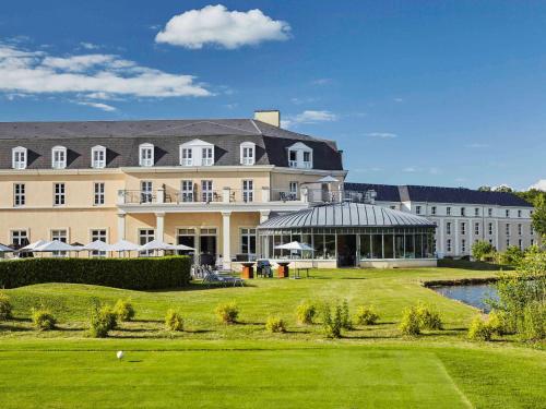 un grand bâtiment avec une pelouse verte devant lui dans l'établissement Mercure Chantilly Resort & Conventions, à Chantilly