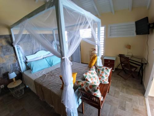 1 dormitorio con cama con dosel y escritorio en Aux Colibris Amoureux : loft de standing avec vue mer en Grand-Bourg
