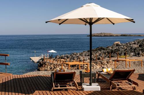 斯塔夫羅斯的住宿－Isla Brown Chania Resort, Curio Collection by Hilton，海滩上遮阳伞下的桌椅