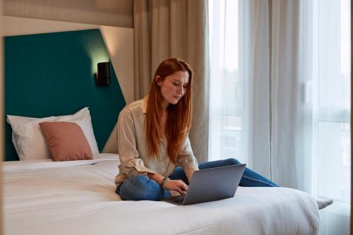 a woman sitting on a bed with a laptop at Aparthotel Adagio Original Toulouse Centre La Grave in Toulouse