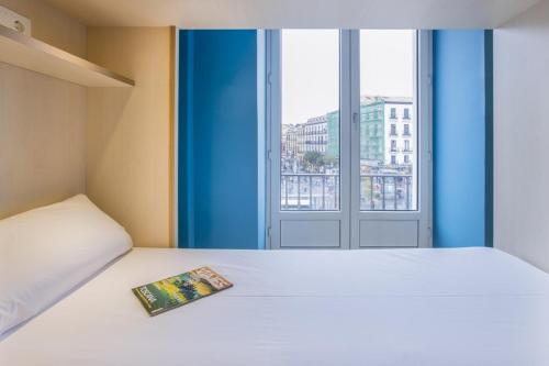 Un dormitorio con una cama blanca con una revista. en Mola Hostel, en Madrid