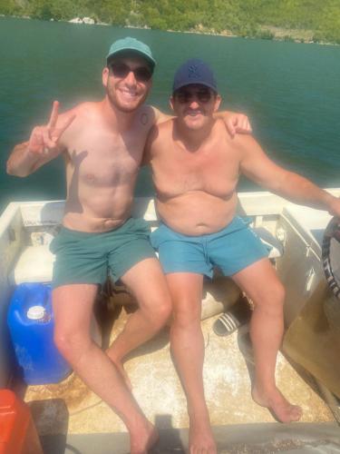 two shirtless men sitting on a boat in the water at Camping Lisna in Vau i Dejës