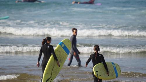 a group of people walking on the beach with surfboards at CHILL SURFER HOSTEL in Tamraght Ouzdar