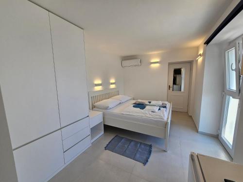 a small white bedroom with a bed and a window at Apartman Velopin in Mali Lošinj