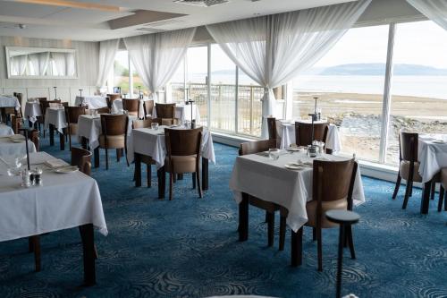 un restaurante con mesas y sillas blancas y ventanas en Redcastle Hotel, en Moville