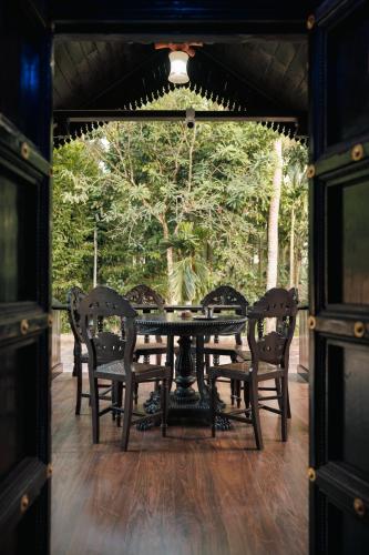 a table and chairs on a porch with trees at Ashriel Farm House by EWA Properties in Kankanādi