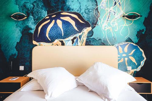 a bed in a bedroom with a painting on the wall at Le Suffren Hôtel in Grimaud