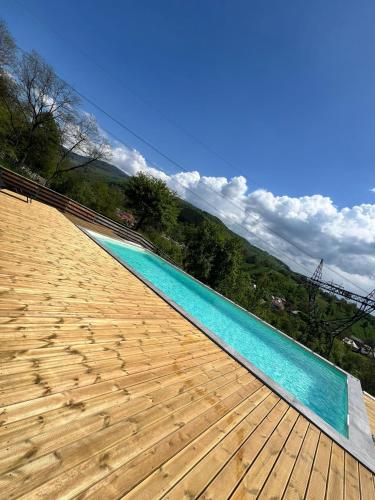 a swimming pool with a wooden deck and blue water at Catunul din Podei Vila Sophia in Dragoslavele