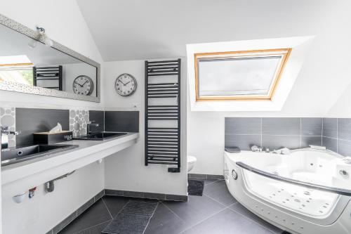 ein Badezimmer mit einer Badewanne, einem Waschbecken und einer Uhr in der Unterkunft Gite Ti Coz piscine intérieure in Caden