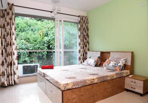 a bedroom with a bed with a large window at Ranghavi sands Apartment with Pool - near beach and Dabolim Airport in Bogmolo