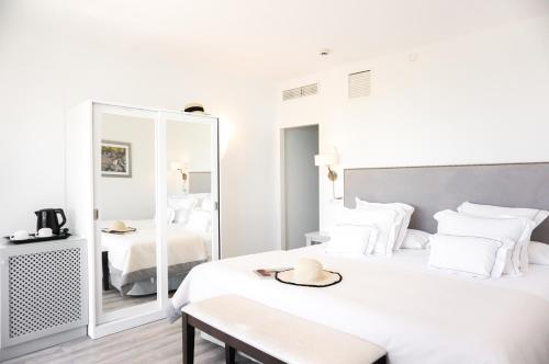 a white bedroom with two beds and a mirror at Hoposa Bahia in Port de Pollensa