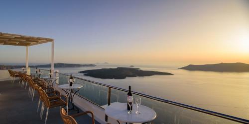una fila de mesas con copas de vino en un balcón con vistas al océano en Vallas Apartments & Villas en Firostefani