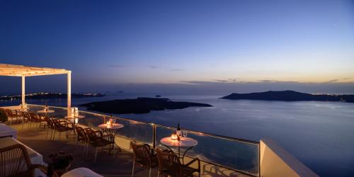un balcón con mesas y sillas y el océano por la noche en Vallas Apartments & Villas, en Firostefani
